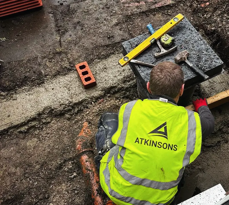ATKINSONS groundworker in branded hi-vis laying drainage on site